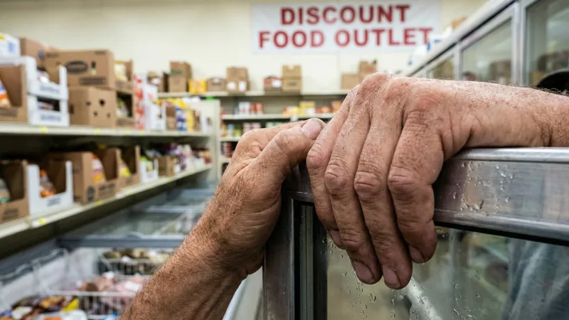 A shopper browsing mismatched shelves of name-brand canned and packaged goods at a bent-n-dent store