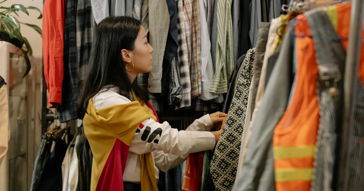 A happy shopper engaging with Thrift Store Pal, browsing colorful clothing racks.